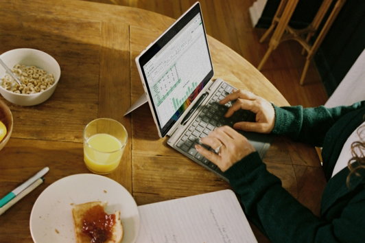 person-working-on-laptop-at-wooden-table-with-breakfast-.jpg Person working on laptop at wooden table with breakfast.